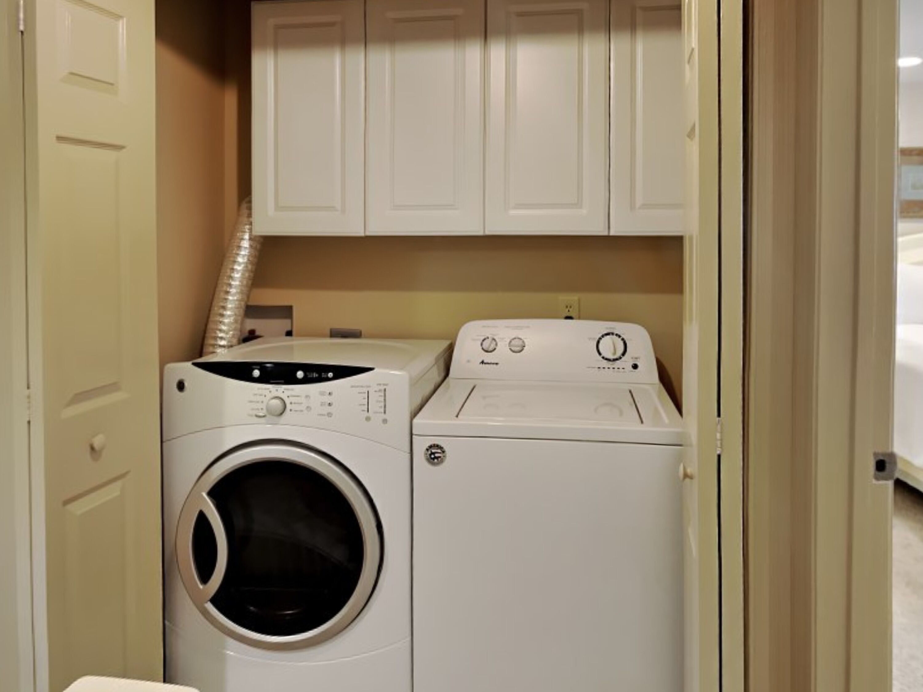 Une petite buanderie équipée de deux machines à laver et deux sèche-linge superposés, avec des placards blancs au-dessus et un mur de couleur beige.
