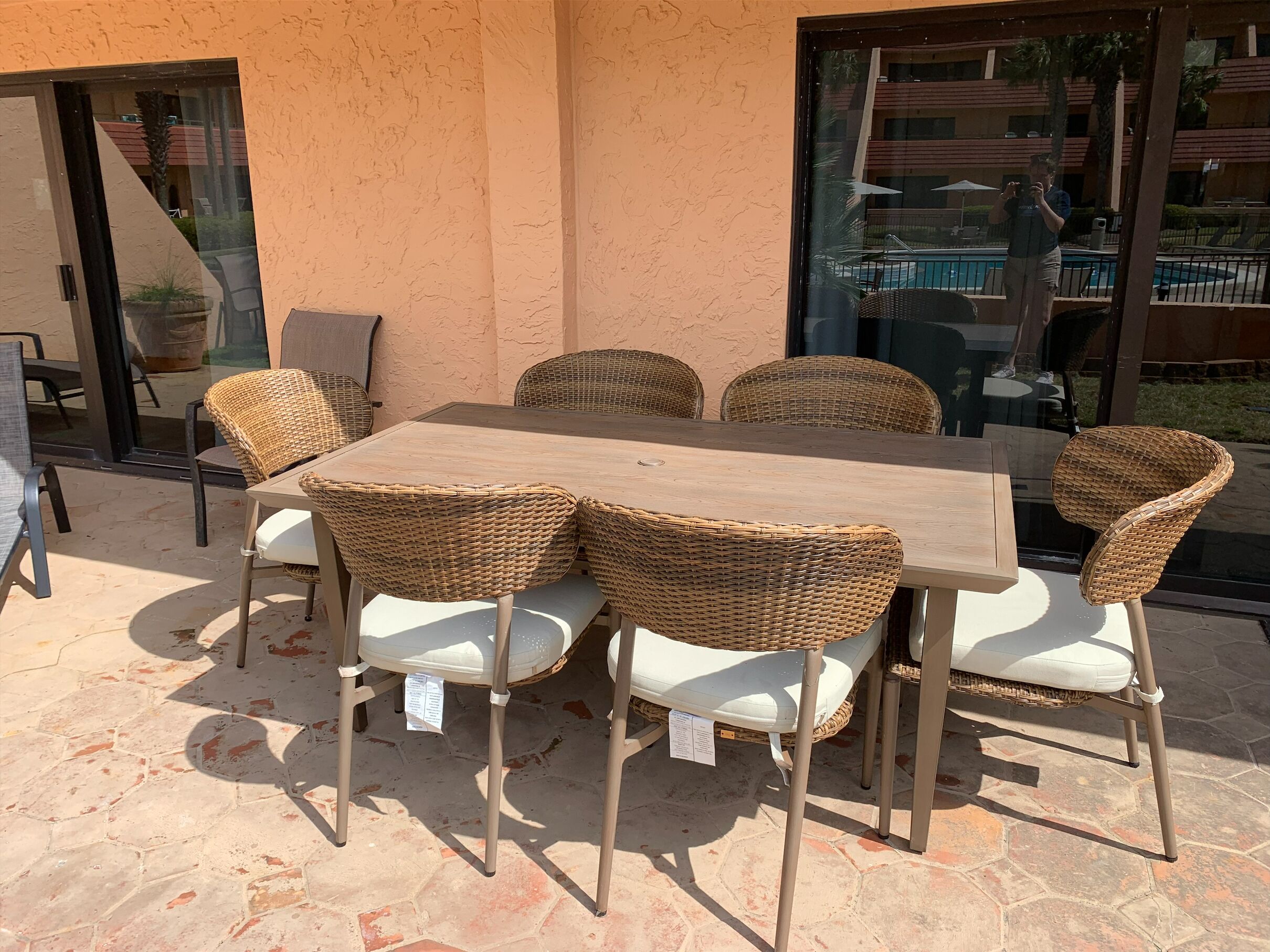 An outdoor patio with a rectangular table and six wicker chairs with white cushions.