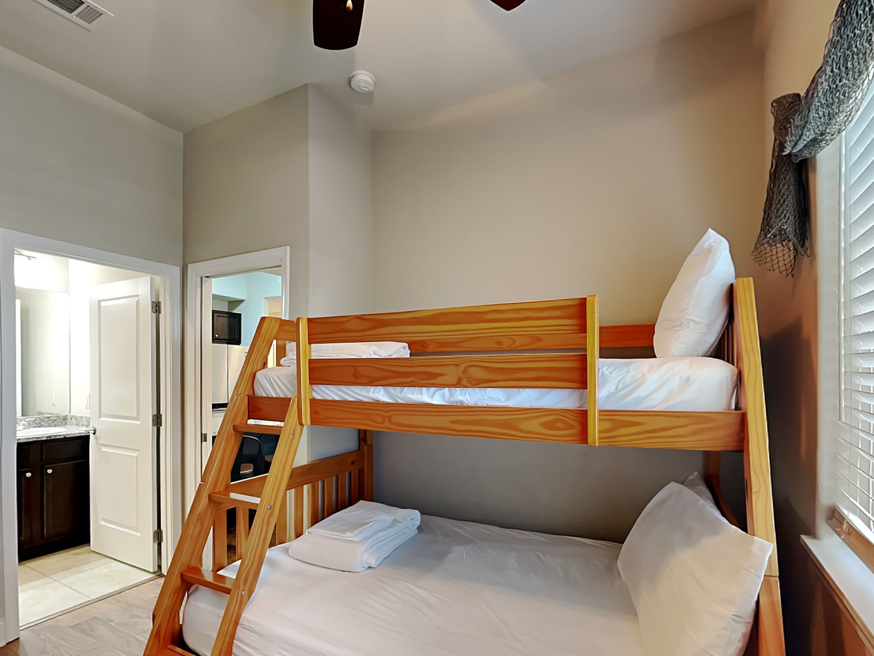A bunk bed with a wooden ladder, white bedding, and a small desk area.