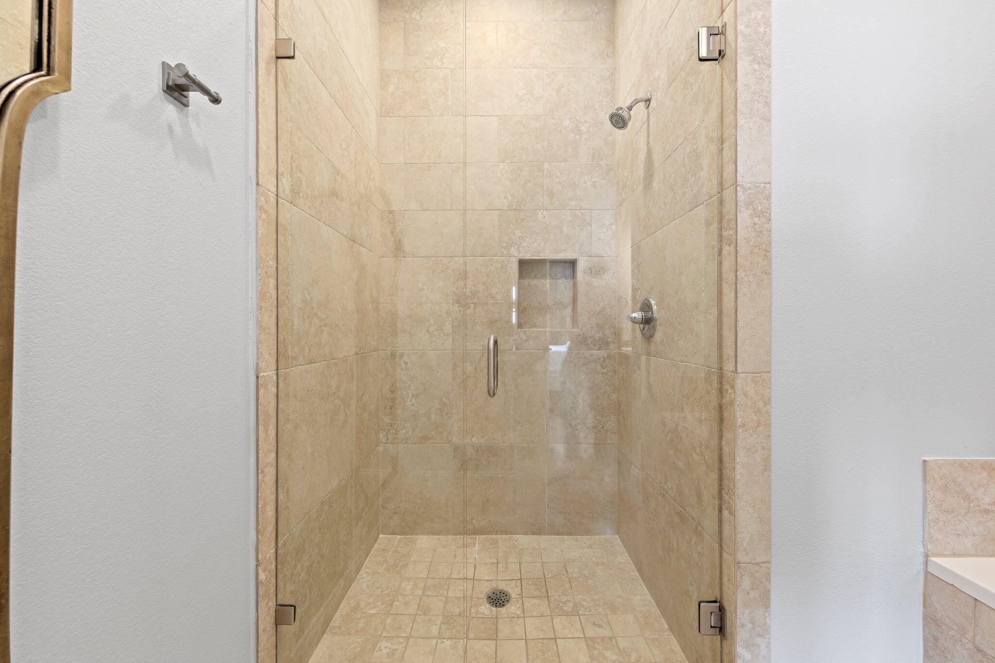 A walk-in shower with beige tiles, a showerhead, and a drain.