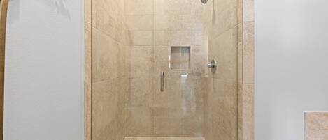 A walk-in shower with beige tiles, a showerhead, and a drain.