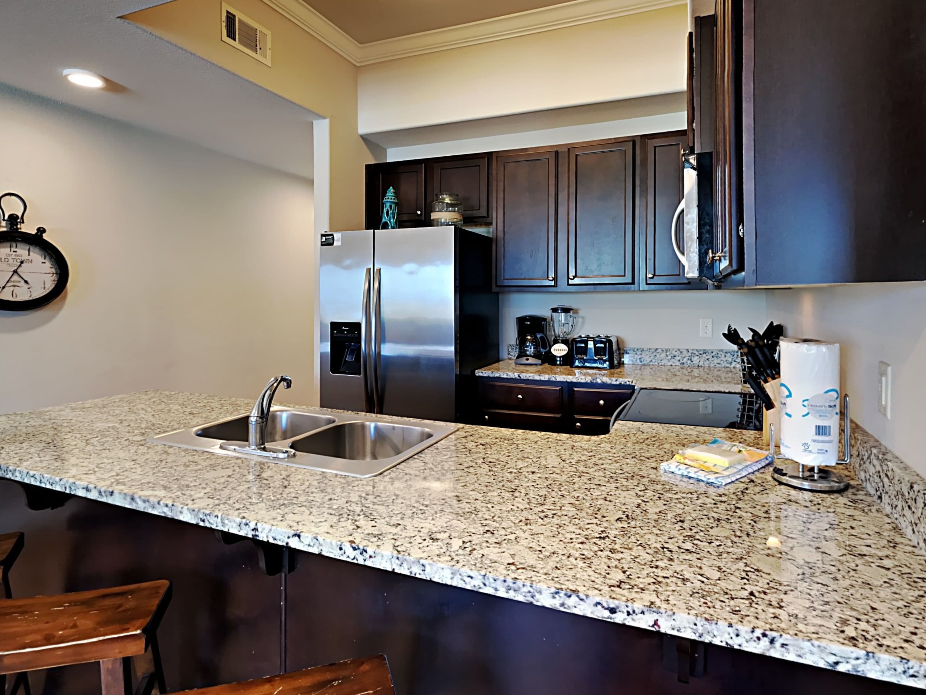 A kitchen with granite countertops, stainless steel appliances, dark wooden cabinets, and a coffee maker.