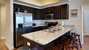 A modern kitchen with dark wood cabinets, stainless steel appliances, granite countertops, and a central island with bar stools. - Alerio by Southern Vacation Rentals (Miramar Beach)