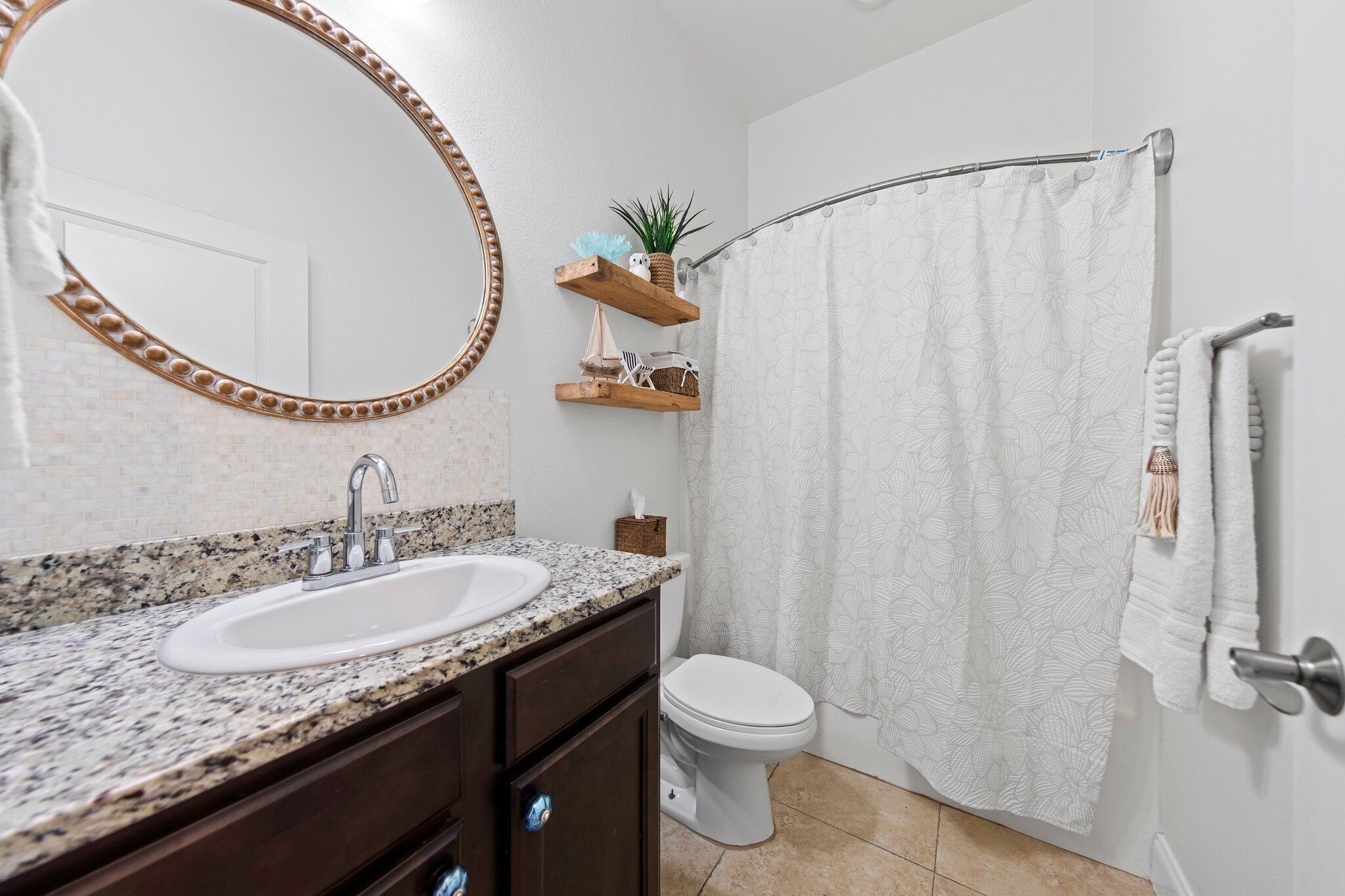 Ein Badezimmer mit Granitwaschtisch, Toilette, Duschvorhang und Handtuchhalter.