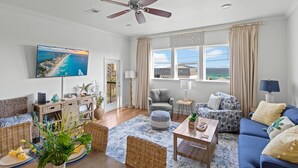 A spacious living room with a large TV, comfortable seating, a ceiling fan, and a view of the ocean. - Alerio by Southern Vacation Rentals (Miramar Beach)