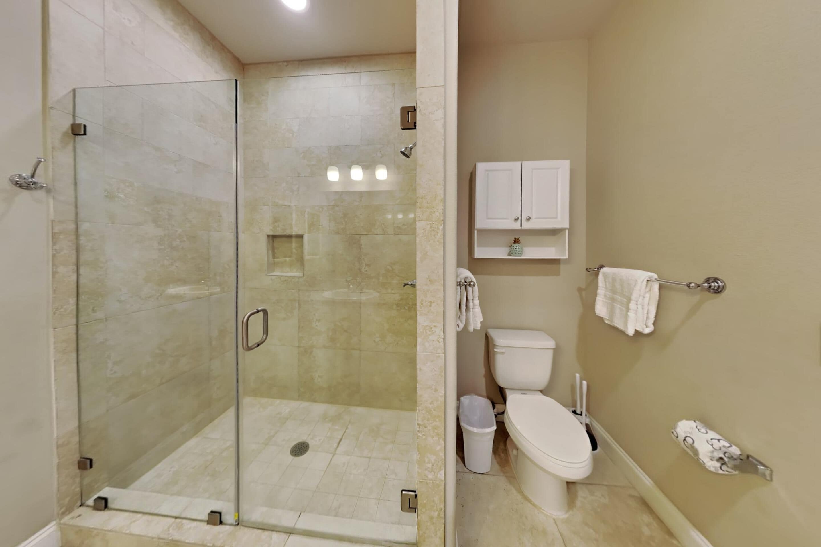 A bathroom with a glass-enclosed shower, a toilet, a sink, and a cabinet.