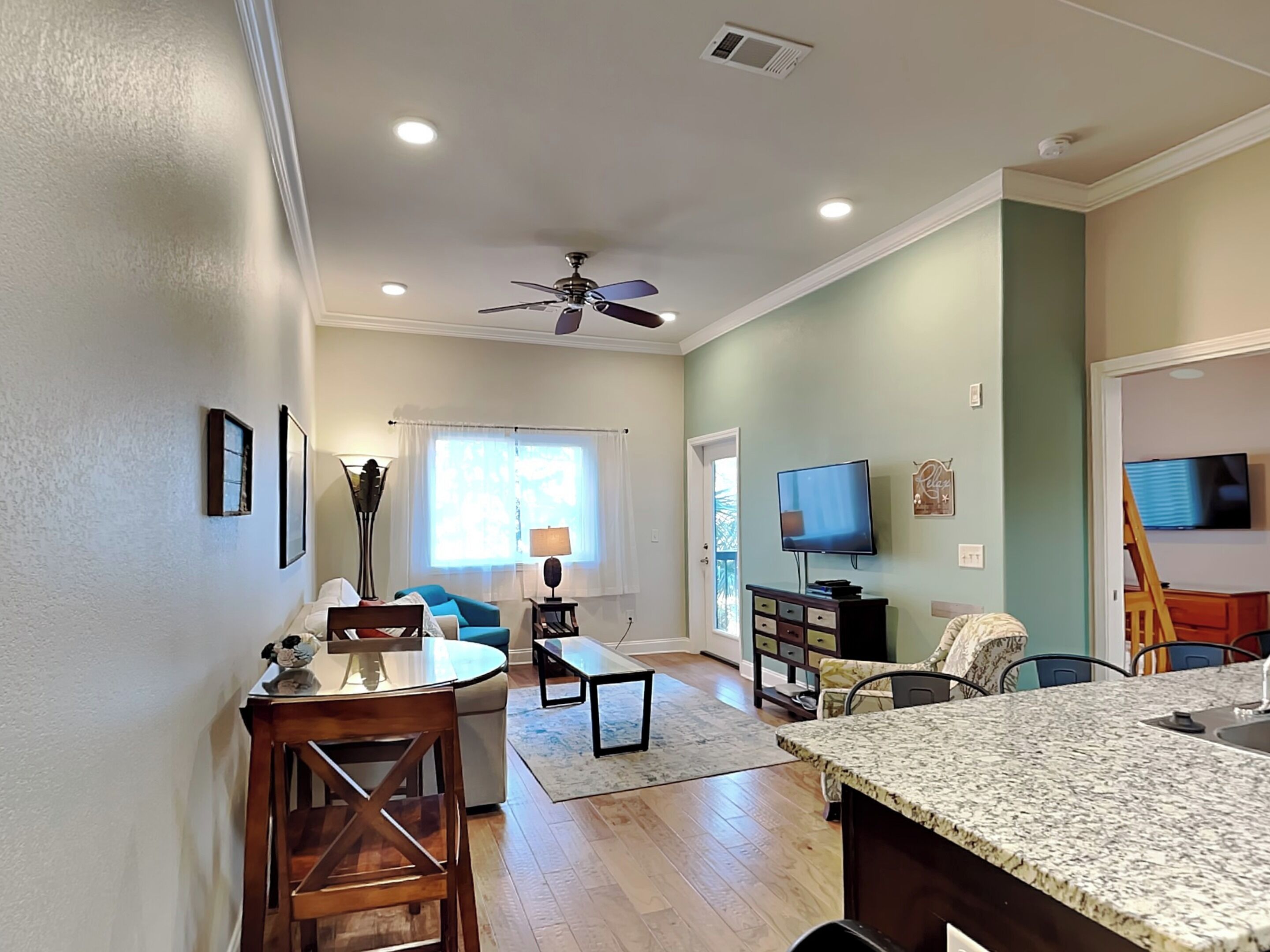 A spacious living area with a dining table, chairs, a sofa, a TV, and a ceiling fan.
