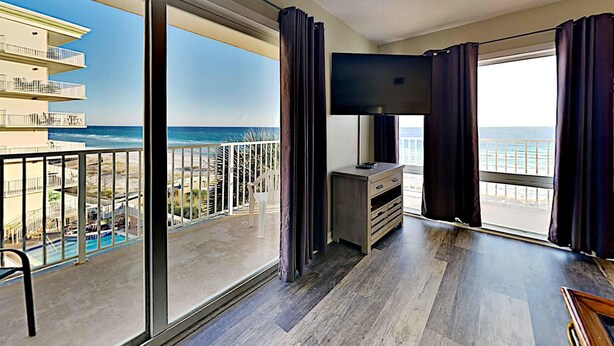 Un balcon spacieux offrant une vue sur la plage et l’océan, un téléviseur à écran plat et un plancher en bois.