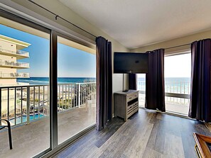 Un balcón amplio con vistas a la playa y al océano, un televisor de pantalla plana y piso de madera.