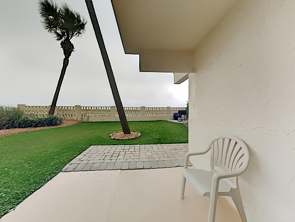 Un patio con una silla de plástico blanca, una palmera y un camino de ladrillo.