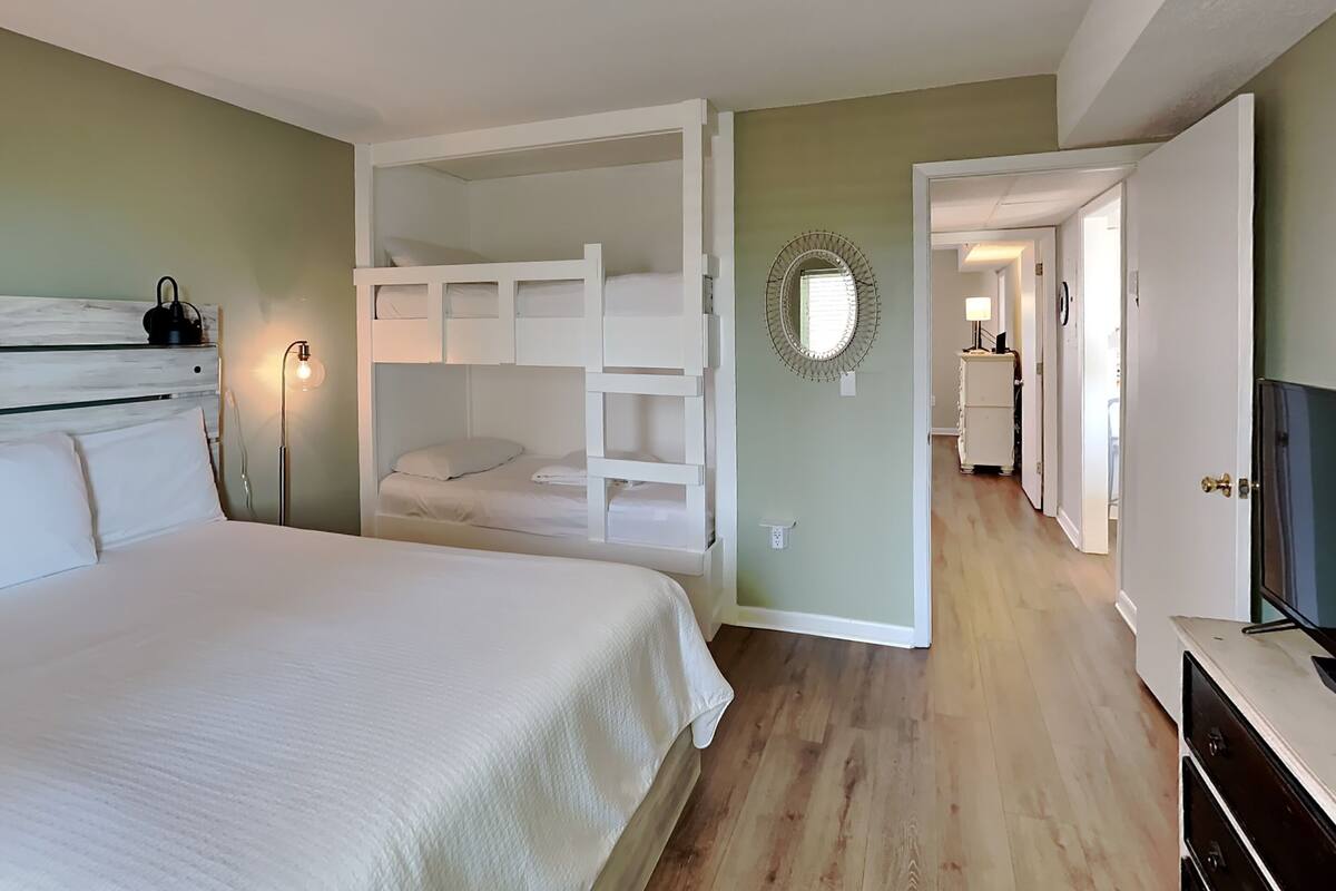 A bedroom with a bunk bed, a bedside lamp, a dresser, and a television.