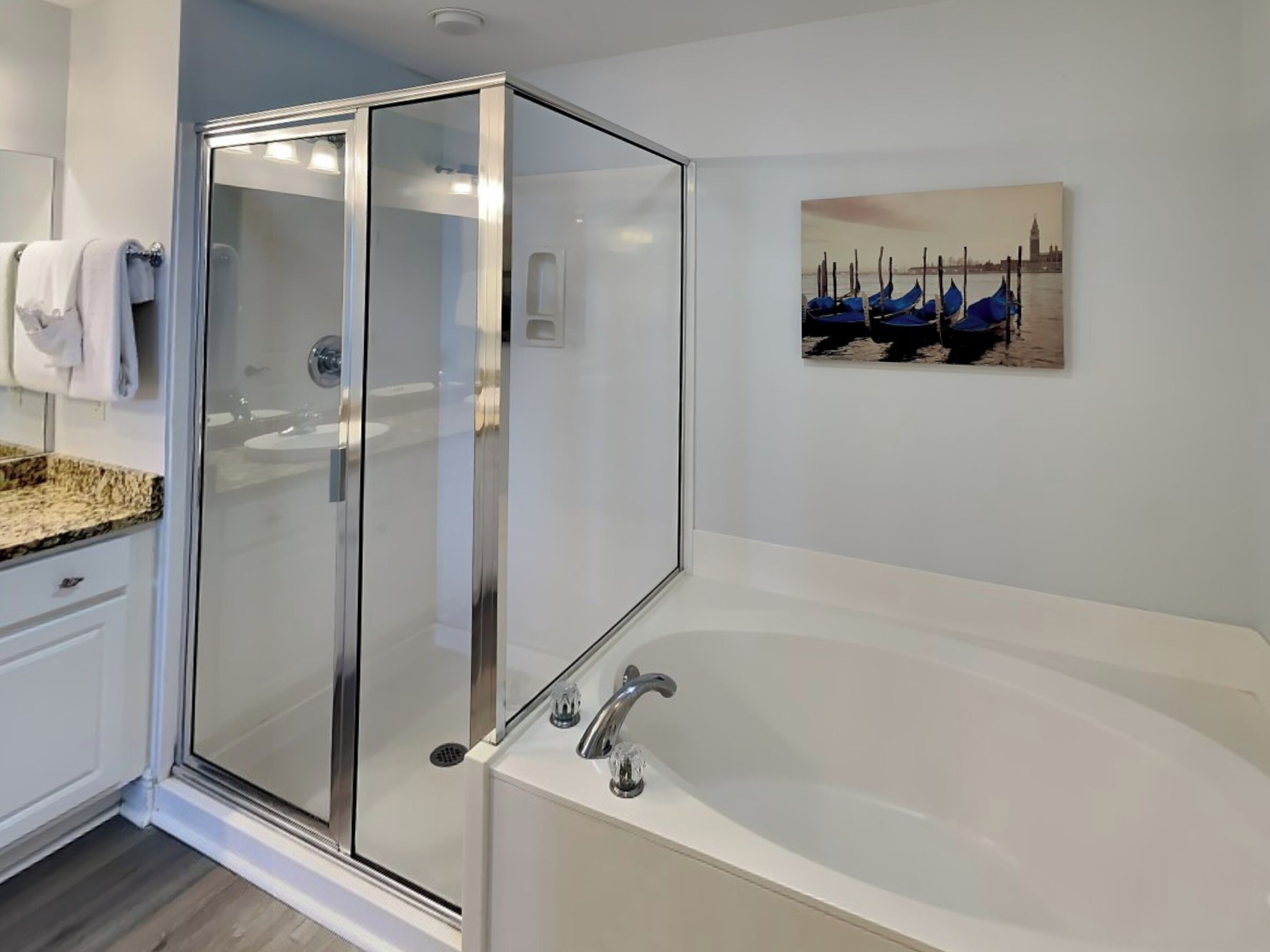 Une salle de bain moderne avec une douche à parois de verre, une grande baignoire et un tableau représentant des bateaux au mur.