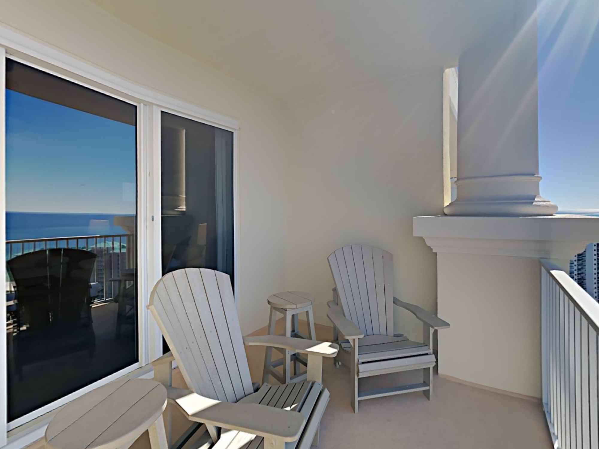 A balcony with two Adirondack chairs and a small table, overlooking a cityscape.