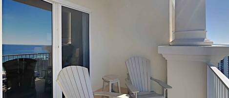 A balcony with two Adirondack chairs and a small table, overlooking a cityscape.