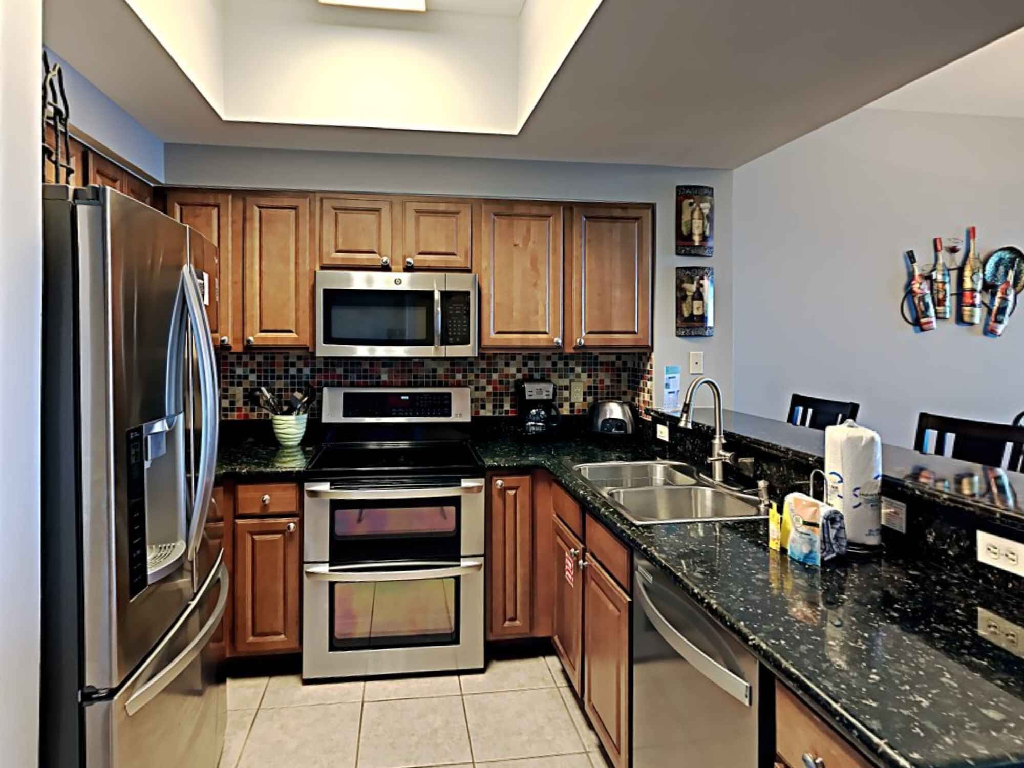 A modern kitchen with stainless steel appliances, wooden cabinets, a tiled backsplash, and a black granite countertop.