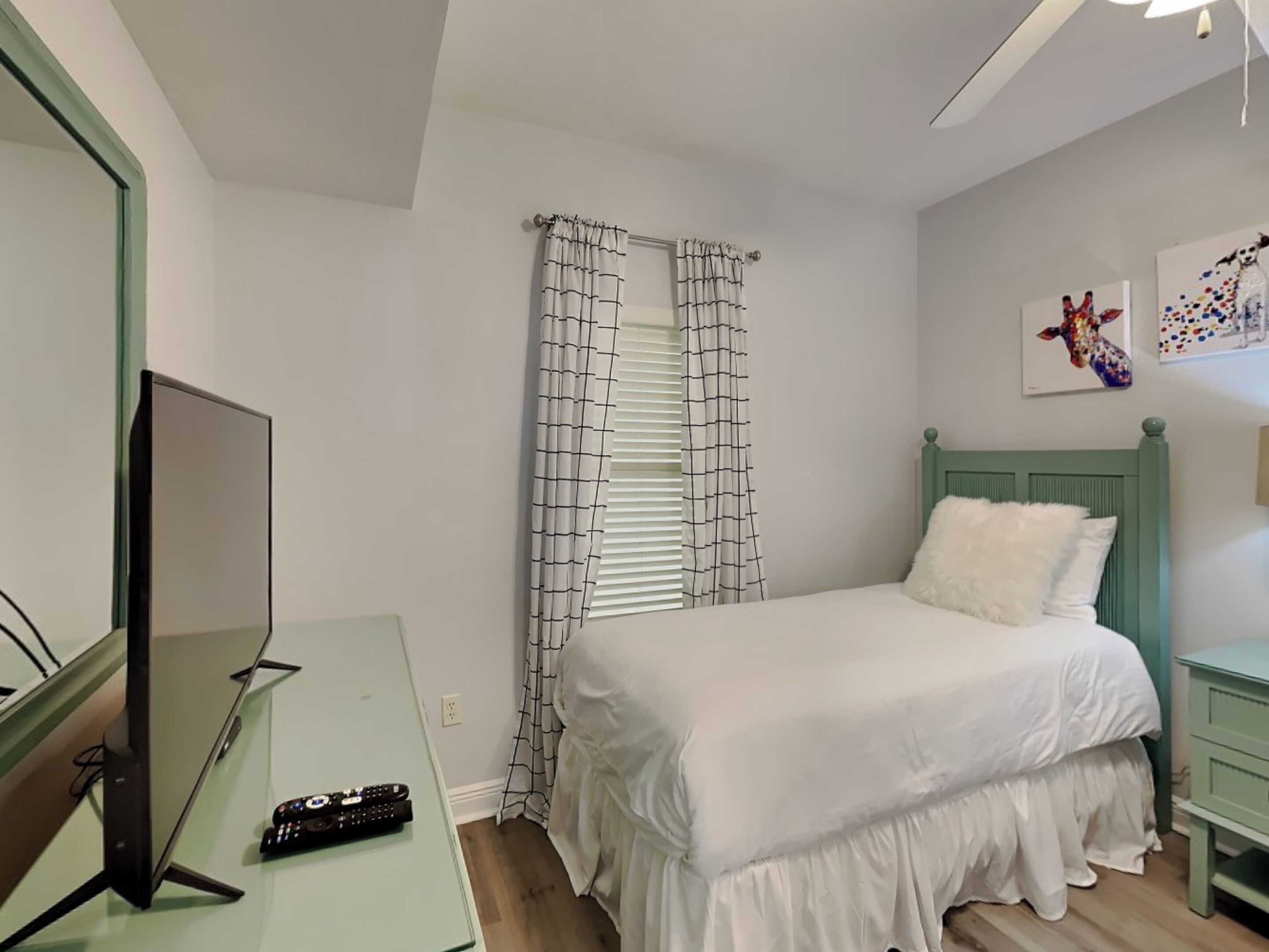 Un dormitorio con una cama, un televisor y un control remoto sobre un mueble.