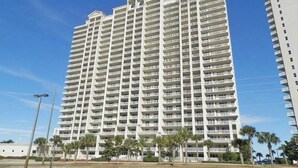 A high-rise hotel with multiple balconies, a flat roof, and a parking lot in front. - Ariel Dunes II by Southern Vacation Rentals (Miramar Beach)