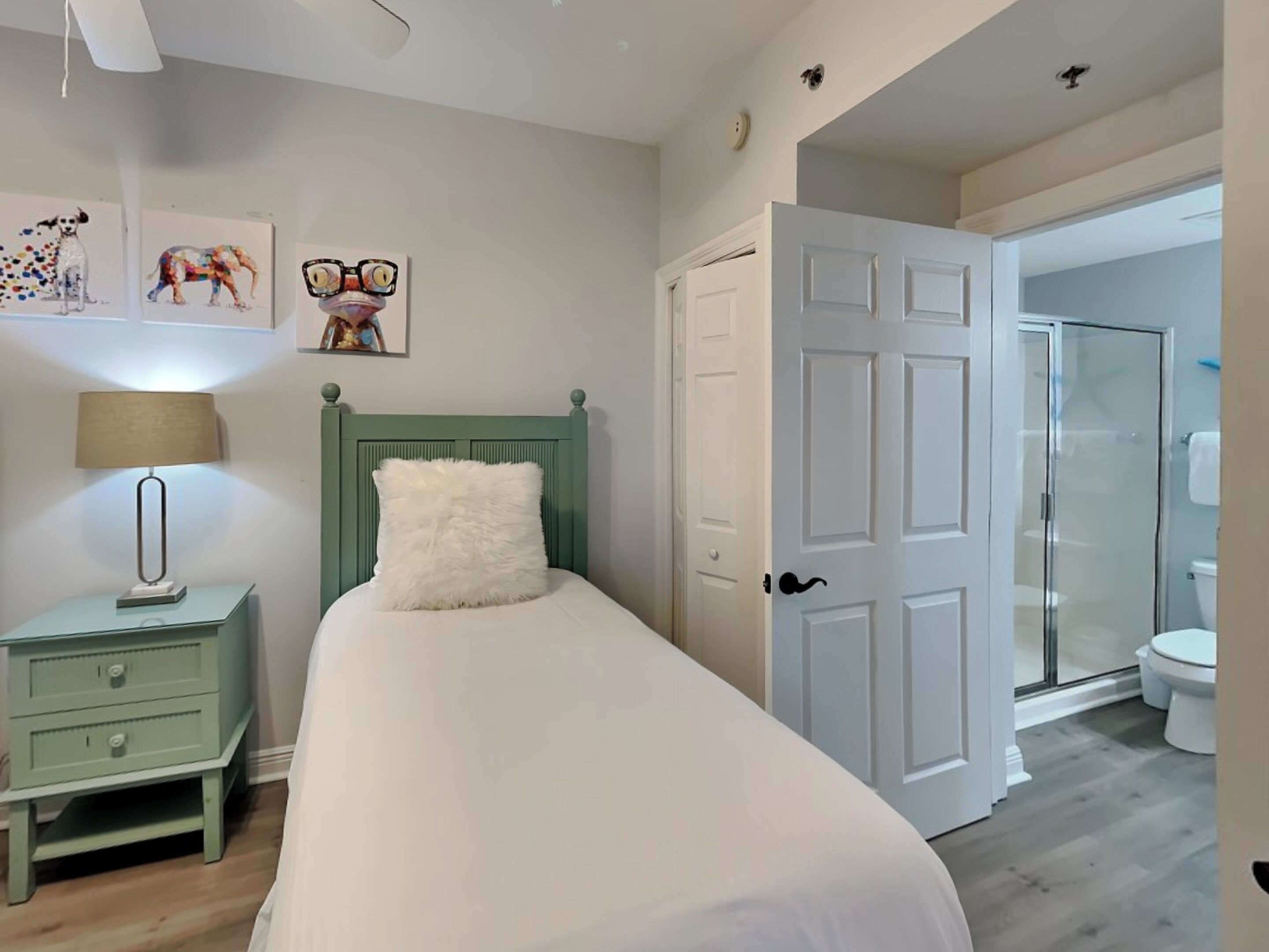 A bedroom with a bed, a nightstand, a lamp, and a door leading to a bathroom.