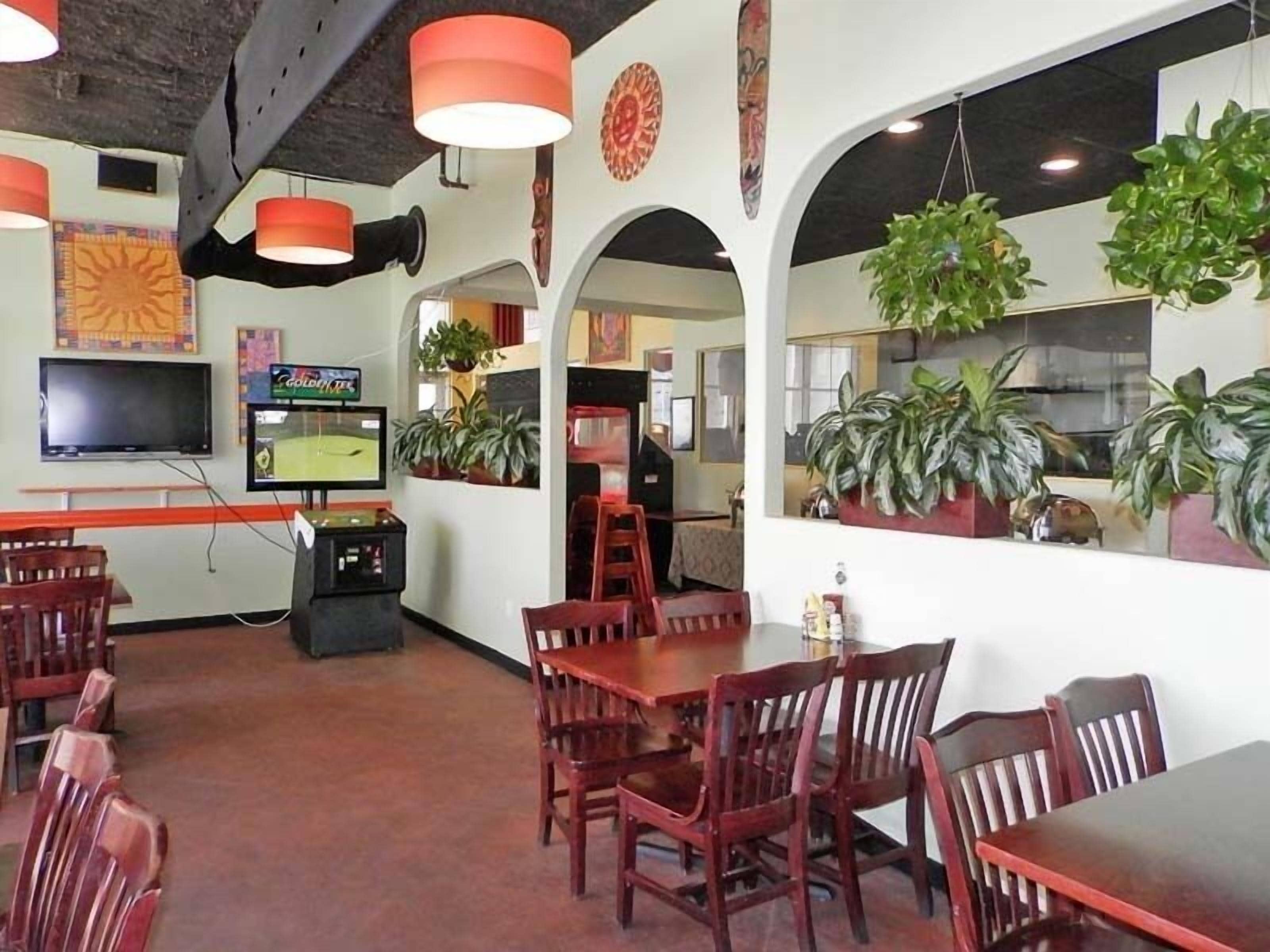 A restaurant interior with wooden tables and chairs, hanging plants, and a television displaying a game.