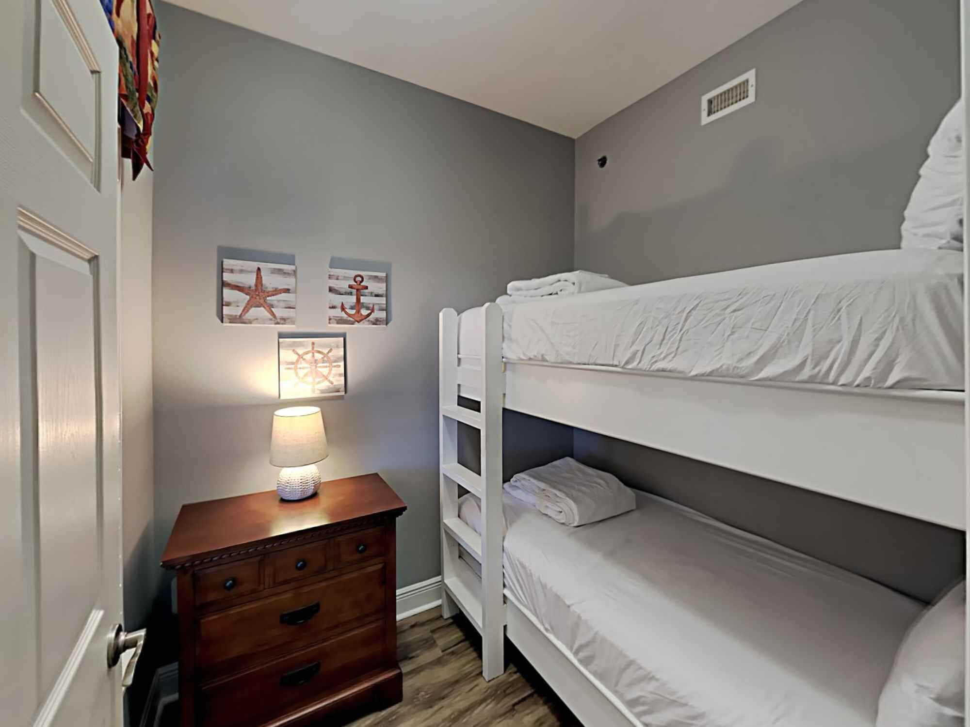 A bedroom with a bunk bed, a wooden dresser, and wall art.