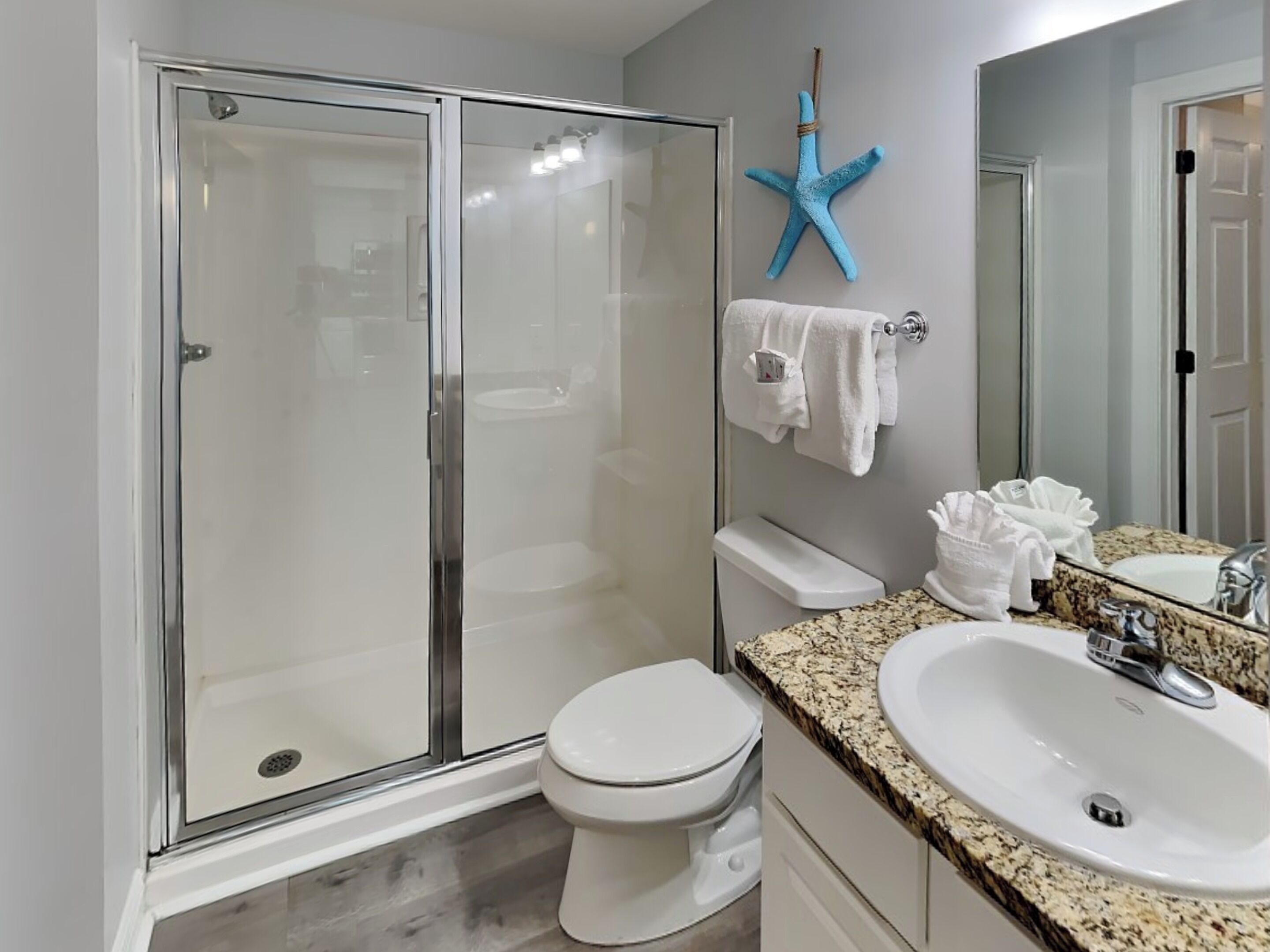A modern bathroom with a glass-enclosed shower, a white toilet, a granite countertop, and a sink with a mirror.