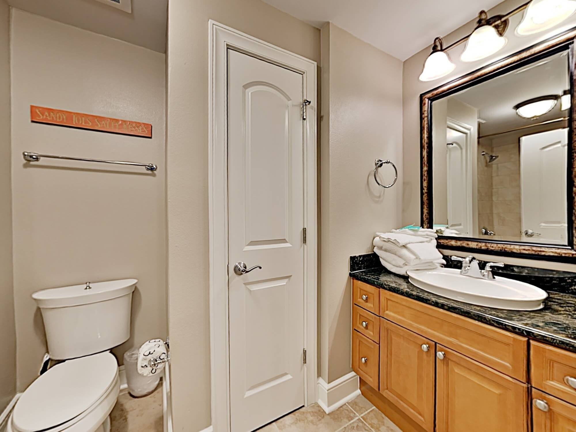 A bathroom with a toilet, sink, vanity, and a large mirror.