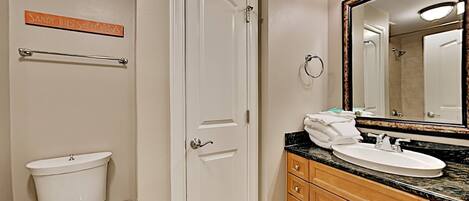 A bathroom with a toilet, sink, vanity, and a large mirror.