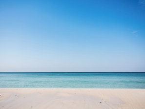 En strand med klart, blåt vand og en sandet kystlinje.