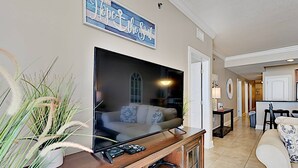 A living room with a flat-screen TV on a wooden entertainment center, a sofa, and a decorative sign above the TV.