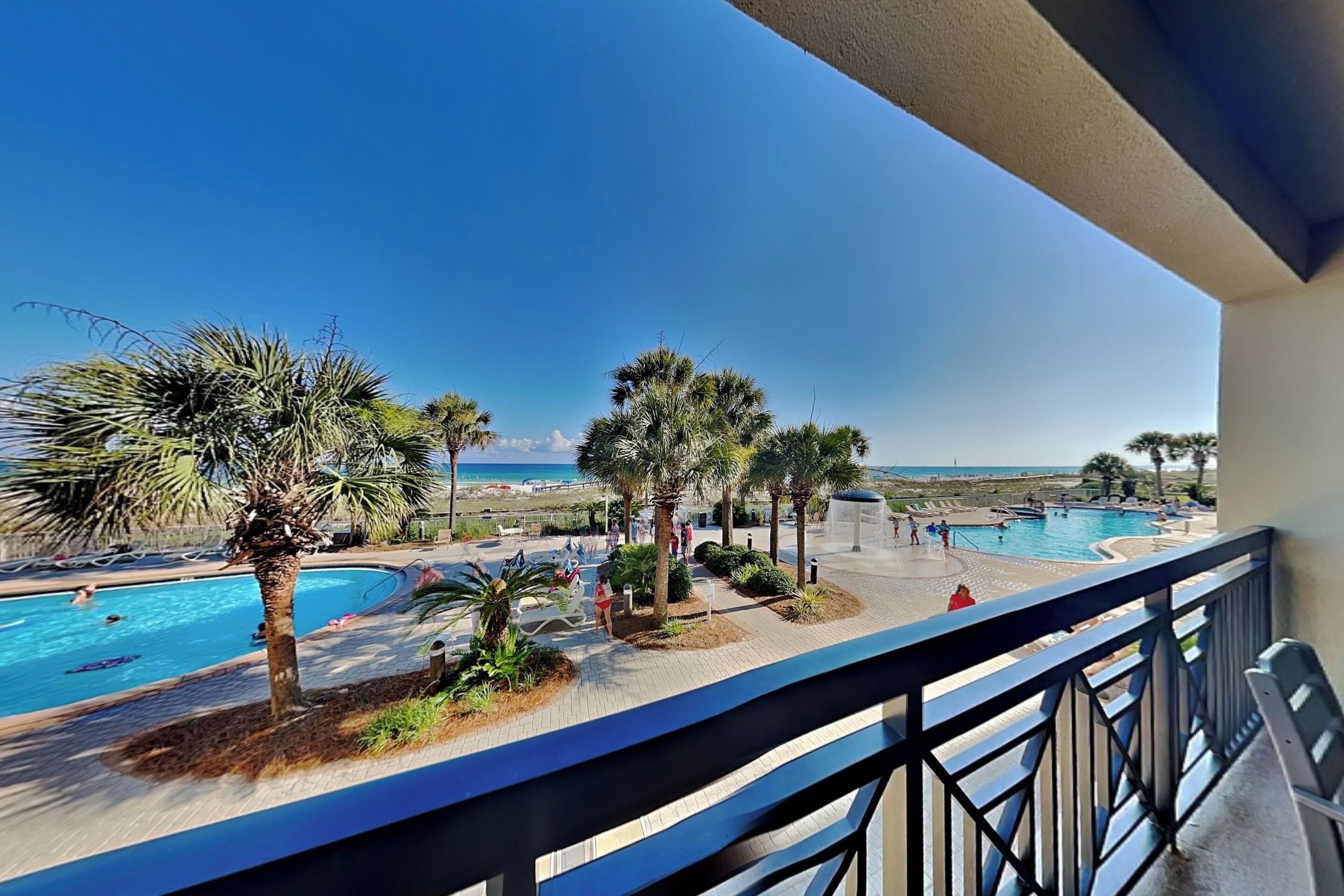 A pool area with palm trees, a clear sky, and a view of the sea.
