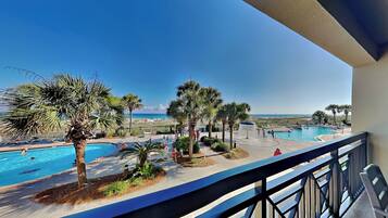 A pool area with palm trees, a clear sky, and a view of the sea.