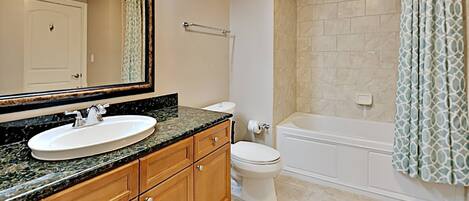 A bathroom with a sink, mirror, vanity, toilet, and bathtub.