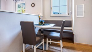 A dining area with a table, two chairs, a bench, a window with a view, and a wall-mounted air vent. - Studio 'Alpen Living 1st Floor Small' with Mountain View, Whirlpool & Wi-Fi (Cadipietra)