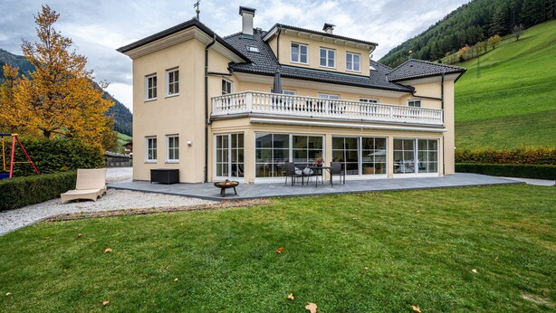 A two-story house with a balcony, a patio with outdoor furniture, and a well-maintained lawn. - Studio 'Alpen Living 1st Floor Small' with Mountain View, Whirlpool & Wi-Fi (Cadipietra)