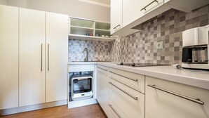 A modern kitchen with white cabinets, a built-in oven, a coffee machine, and a checkered backsplash. - Studio 'Alpen Living 1st Floor Small' with Mountain View, Whirlpool & Wi-Fi (Cadipietra)