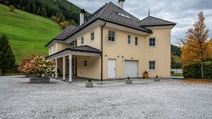 A two-story house with a covered porch, a garage, and a gravel driveway. - Studio 'Alpen Living 1st Floor Small' with Mountain View, Whirlpool & Wi-Fi (Cadipietra)