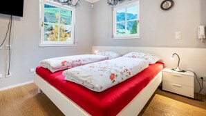 A bedroom with two beds, a bedside table, a lamp, and a view of a green landscape through the windows. - Studio 'Alpen Living 1st Floor Small' with Mountain View, Whirlpool & Wi-Fi (Cadipietra)
