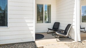 Un porche abrité avec deux chaises et une petite table, un revêtement extérieur blanc et une fenêtre avec des stores.