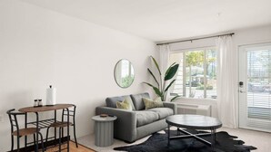 Un salon moderne avec un canapé gris, une table basse ronde, une petite table d’appoint et un tapis en cuir noir.