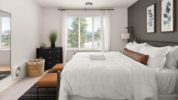 Une chambre à coucher moderne avec un grand lit, une commode, une fenêtre avec des rideaux et une vue sur l’extérieur.