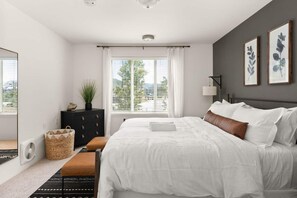 A modern bedroom with a large bed, a dresser, a window with curtains, and a view of the outdoors.