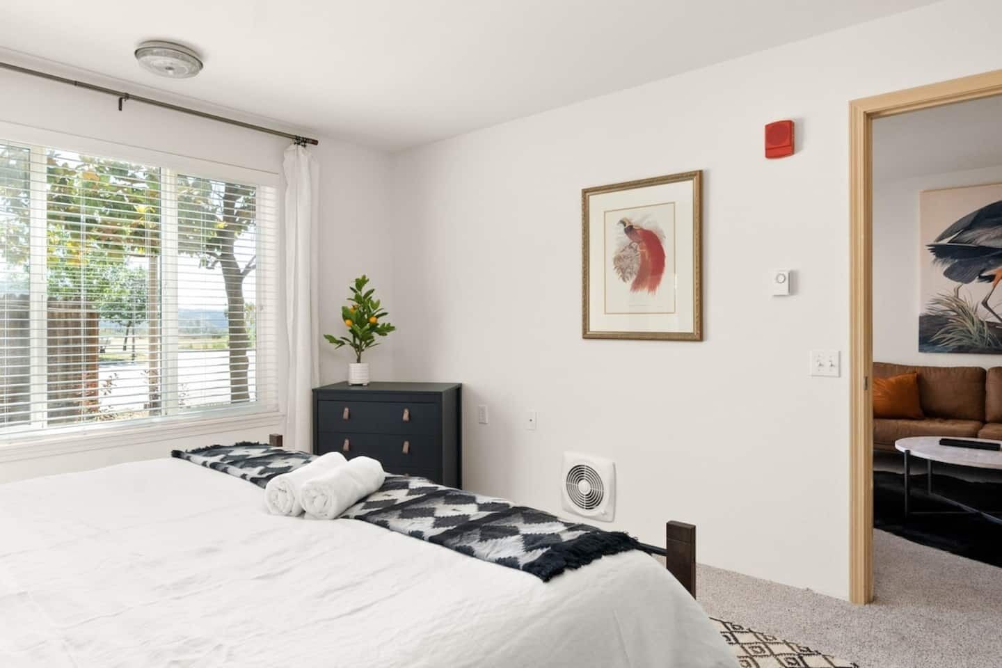 A bedroom with a bed, a dresser, a fan, and a painting on the wall.
