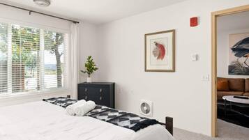 A bedroom with a bed, a dresser, a fan, and a painting on the wall.