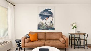 A living room with a brown sofa, a round coffee table, a side table, a painting of a bird, and a small round table with chairs.