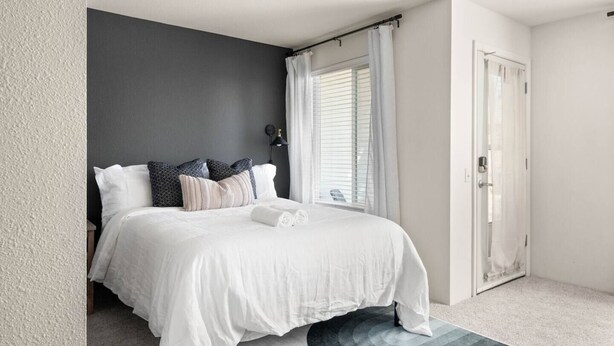 A bedroom with a bed, a dark wall, a window with curtains, and a door. - The Trinity | Studio in Paradise (Paradise)