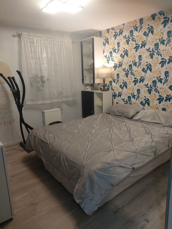 A bedroom with a bed, a bedside table, a mirror, a radiator, and a floral wallpaper.