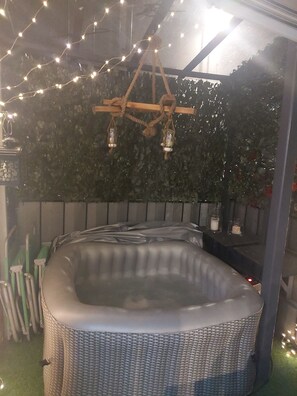 A hot tub with a wicker exterior, surrounded by a wooden deck and a green wall.
