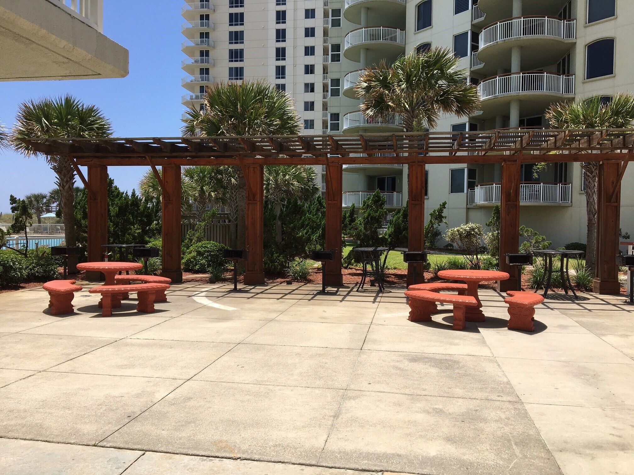 An outdoor patio area with wooden pergola, red stone tables, and benches.