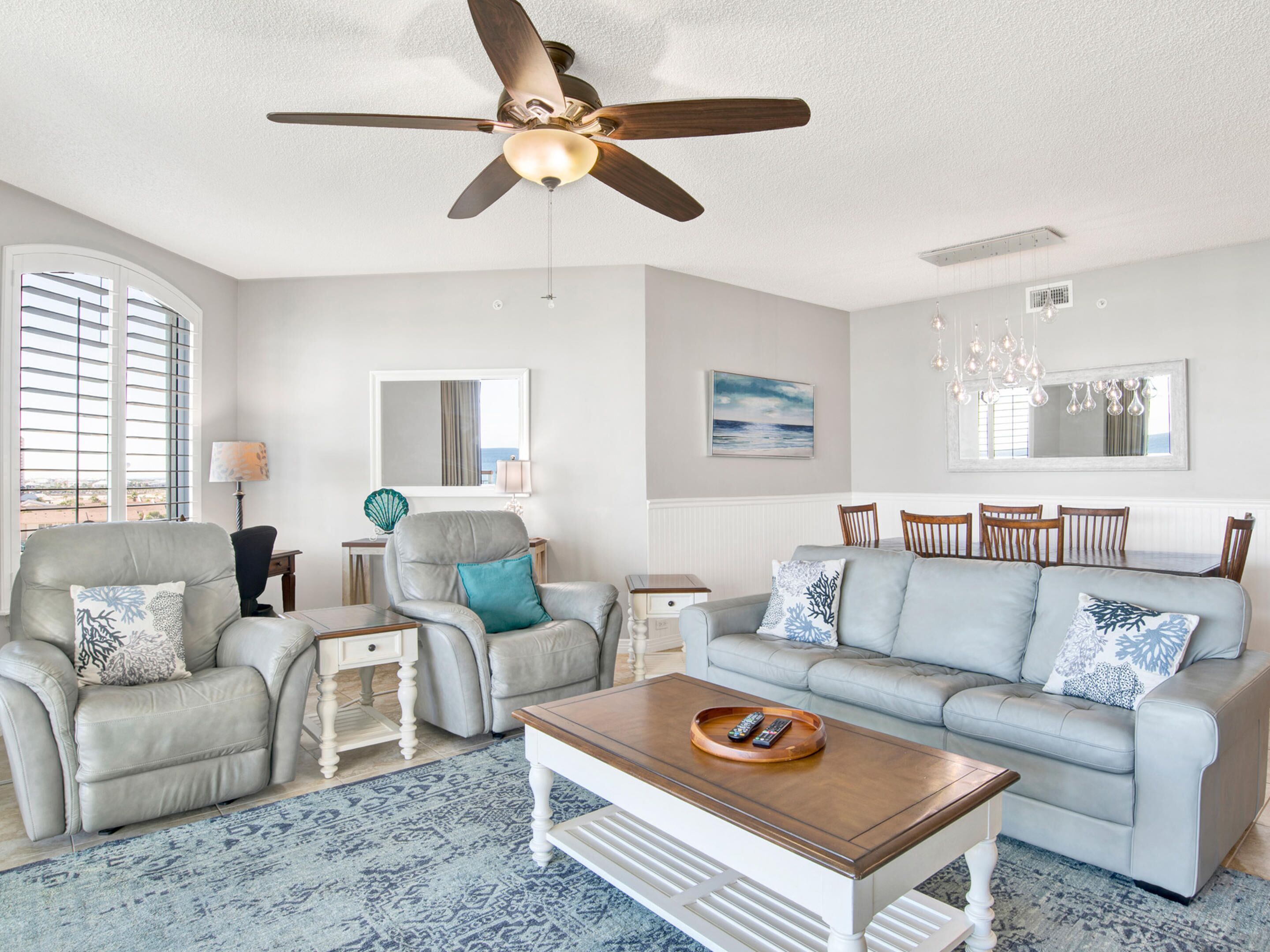 A living room with a ceiling fan, a sofa set, a coffee table, and a dining area with chairs.