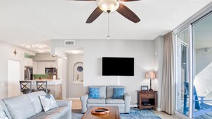Una sala de estar moderna con ventilador de techo, televisor de pantalla plana, sofá, mesa de centro y vistas al exterior.